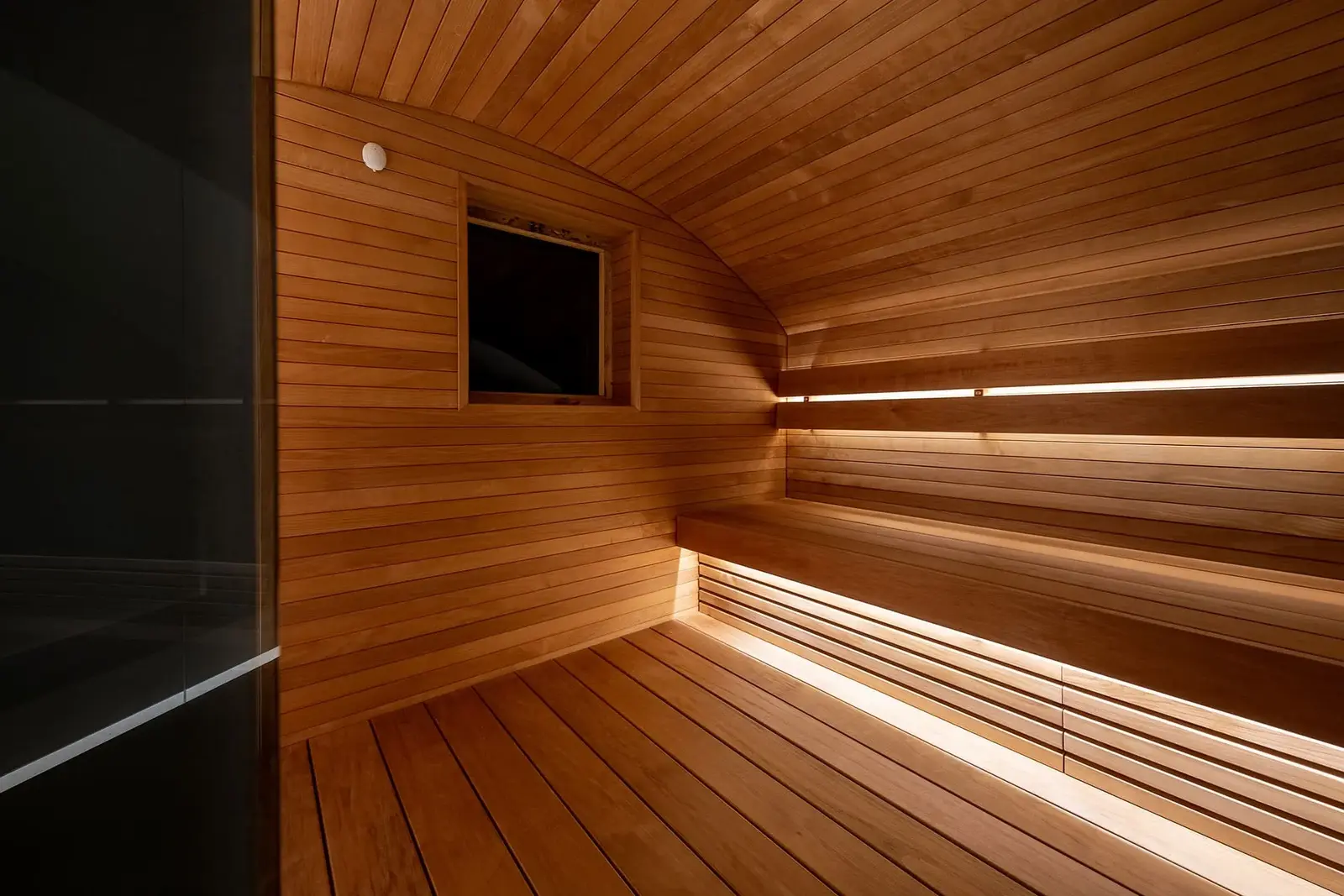 Sauna with an arched ceiling lined in horizontal Thermory STS4 thermo-aspen boards, with benches lit from below